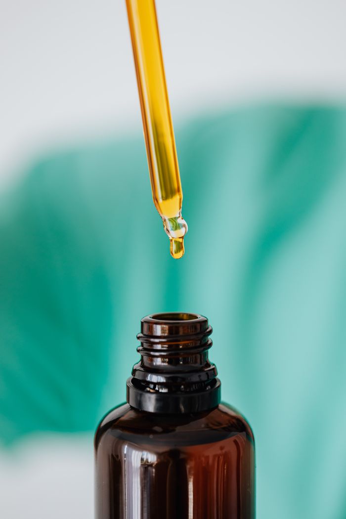 A dropper releasing oil into an amber bottle with a green background, showing skincare or essential oils concept.